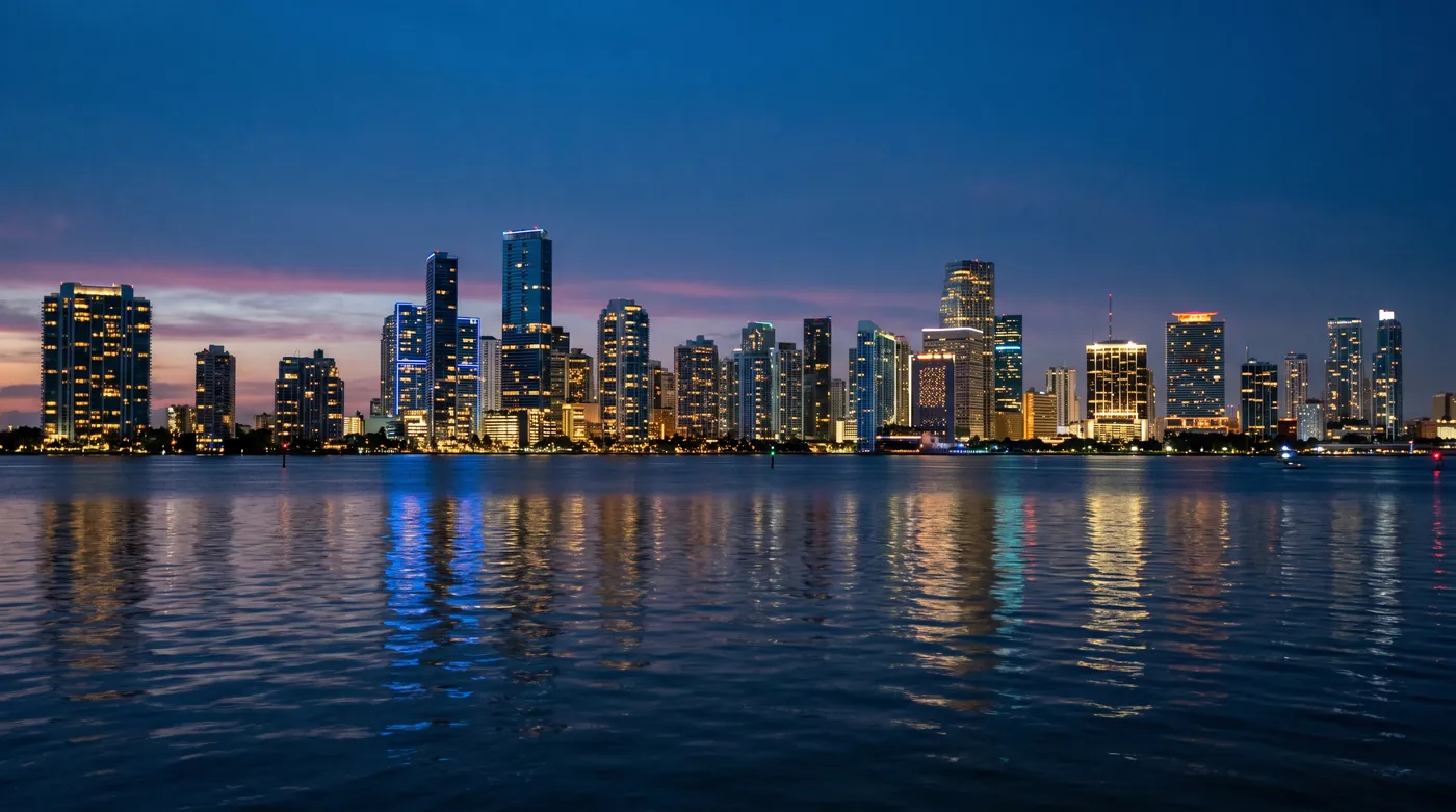 The Miami skyline at blue hour across still water, lit towers and their reflections.