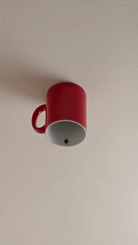 Close on the red mug upside down on a textured white ceiling, still full.