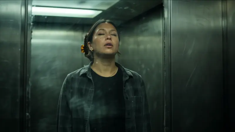 The character alone in a dim steel elevator, eyes closed.