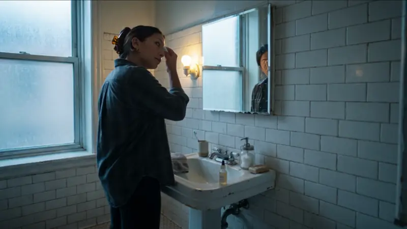 The same persona at a white bathroom sink beside a window.