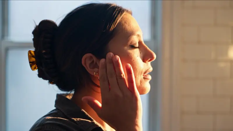 The same persona in profile in warm window light, hand against her cheek.