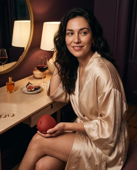 A woman in a champagne silk robe at a vanity with the RASA object in her palm.